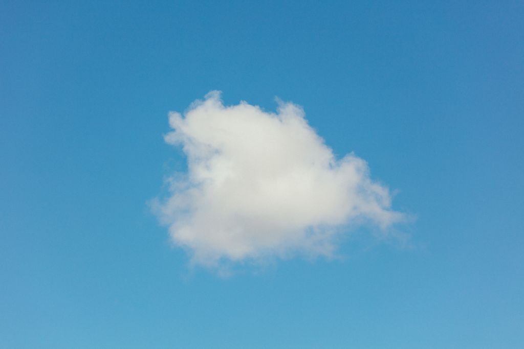 A single cumulus cloud floats peacefully against a vivid blue summer sky.